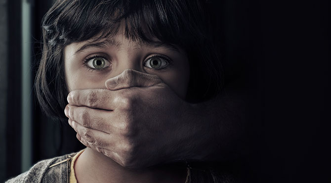 Fotografía de niña con la boca tapada por una mano adulta